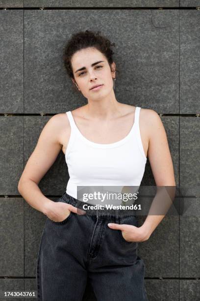 woman standing with hands in pockets near gray wall - camiseta de tirantes fotografías e imágenes de stock