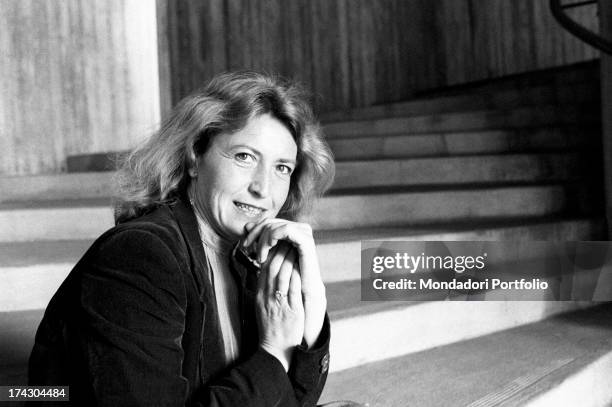 Italian writer and journalist Barbara Alberti smiling with her hand on her chin sitting on a staircase. 1970s.