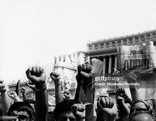 Crowd doing the clenched fist salute for Enrico Berlinguer's coffin. A person showing the first page of the newspaper L'Unità with a picture of the...