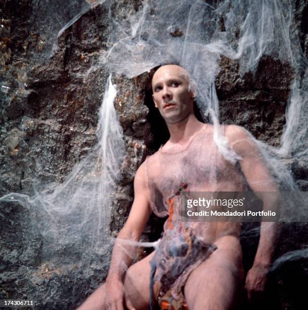 Bare chested athletic man seated on the rocks of the scenography during the filming of Roger Vadim's Barbarella; he's one of the prisoners of the...