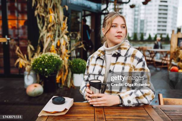 calm blonde woman drinking coffee from travel mug in sidewalk cafe outdoors in western europe - reusable cup stock pictures, royalty-free photos & images