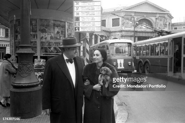 The US film director Orson Welles, with a cigar in his mouth and a large hat on his head, walks arm in arm with his third wife, the Italian actress...