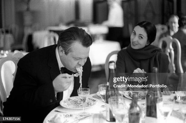 The US film director Orson Welles, eats a plate of spaghetti with tomato sauce in front of a bottle of water and red wine, while his third wife, the...