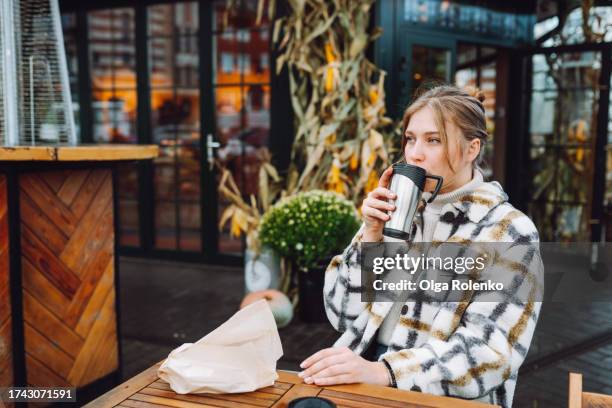 enjoying the outdoors with coffee: blonde woman sips from a travel mug at a sidewalk cafe on her lunch break - travel mug stock pictures, royalty-free photos & images