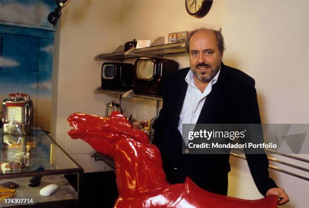 The Italian stylist Elio Fiorucci poses resting his left hand on a sculpted red horse. 1994..