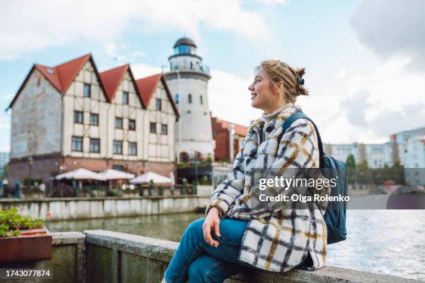 young woman, tourist rest on waterfront against lighthouse and row houses on quayside - one embankment stock pictures, royalty-free photos & images