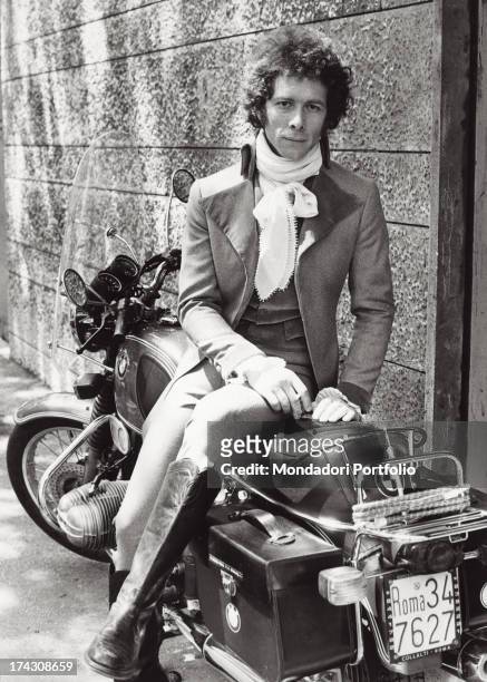 Italian actor Gabriele Lavia sitting on a motorcycle and having rest on the set of a film. Rome, 1970s.