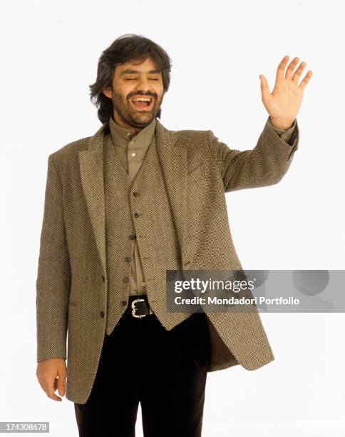 The Italian tenor Andrea Bocelli is dressed in an elegant gray suit, making a gesture of greeting. Italy, 1995..