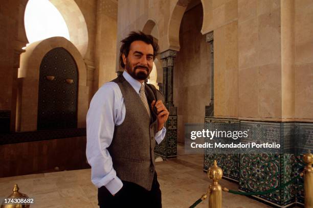 The Indian actor Kabir Bedi looks at the camera smiling, with the jacket over his shoulder, within the newly built Mosque of Hassan II; he's in...