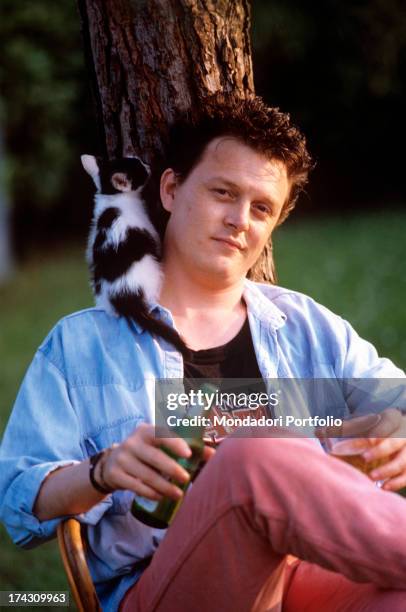 The Italian singer-songwriter Zucchero, Adelmo Fornaciari's pseudonym, drinks a beer leaning against a tree with a little cat on his shoulder. Italy,...