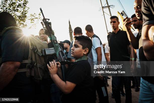 Young boy help carry an assault rifle belonging to an older fighter as others support for the Palestinians killed in an Israeli assault on the Nour...