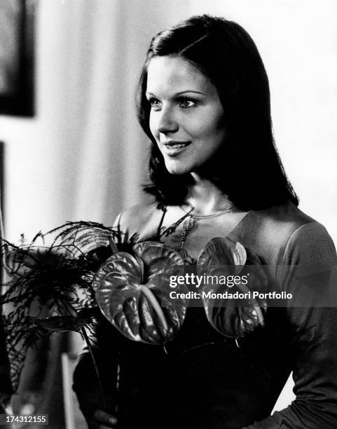 Italian actress Agostina Belli smiling holding a plant in The Governess. Rome, 1974.