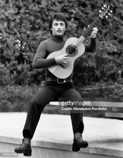 Italian actor, singer and songwriter Tony Renis jumping down from a low wall playing the guitar. Italy, 1972.