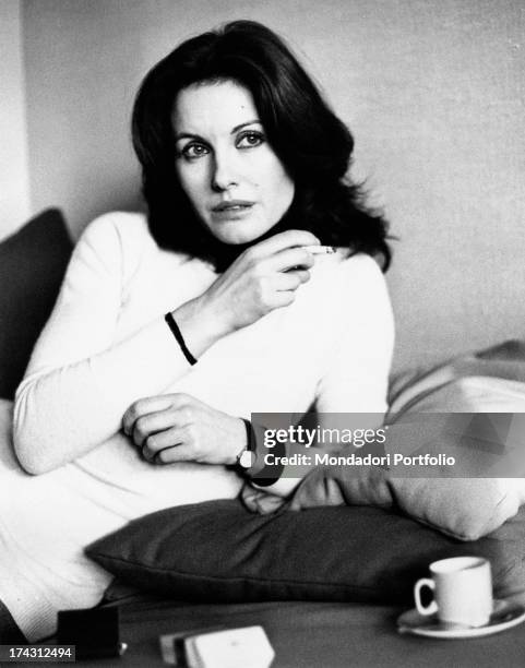 Italian television presenter and actress Gabriella Farinon smoking a cigarette lying on the sofa. Rome, 1970s.