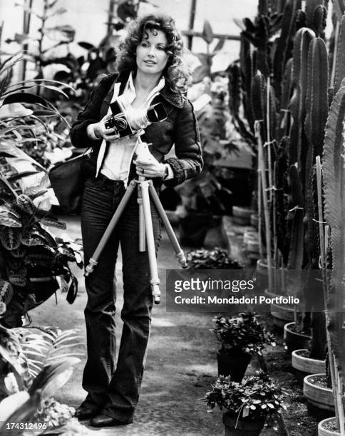 Italian television presenter and actress Gabriella Farinon walking in a glasshouse with a camera in her hands. Rome, 1970s.