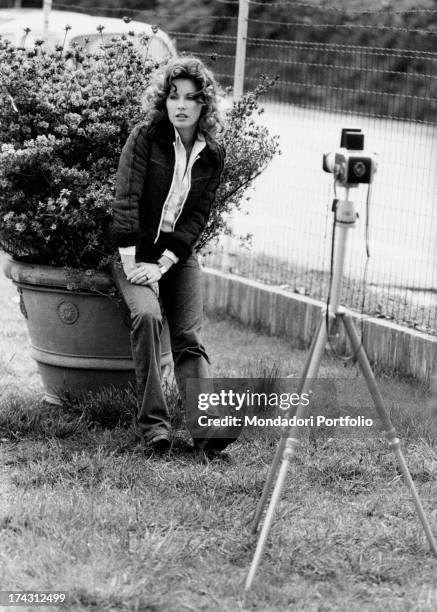 Italian television presenter and actress Gabriella Farinon sitting on a flowerpot in a garden. Rome, 1970s.