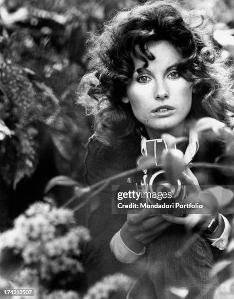 Italian television presenter and actress Gabriella Farinon, in a glasshouse, holding a camera in her hands. Rome, 1970s.