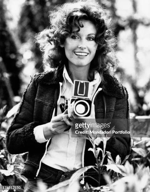 Italian television presenter and actress Gabriella Farinon smiling in a garden with a camera in her hands. Rome, 1970s.