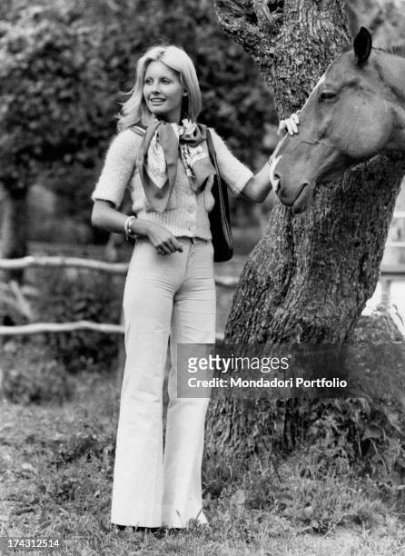 Italian television presenter and actress Gabriella Farinon petting the muzzle of a horse. 1970s.