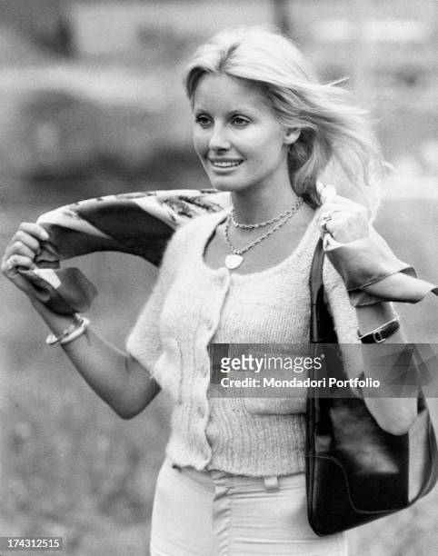 Italian television presenter and actress Gabriella Farinon adjusting a scarf on her shoulders. 1970s.