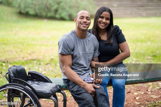 portrait of man in wheelchair and his wife in a public park - paralysis stock pictures, royalty-free photos & images