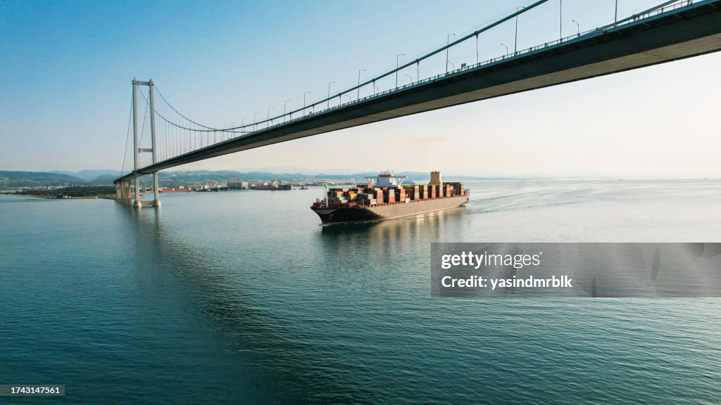 Tiro de drone de grande navio de carga transportando contêineres passando sob a ponte