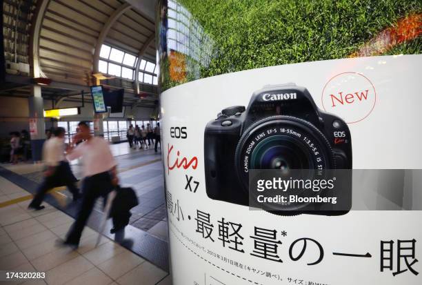 Pedestrians walk past an advertisement for the Canon Inc. EOS Kiss X7 digital single-lens reflex camera in Tokyo, Japan, on Tuesday, July 23, 2013....