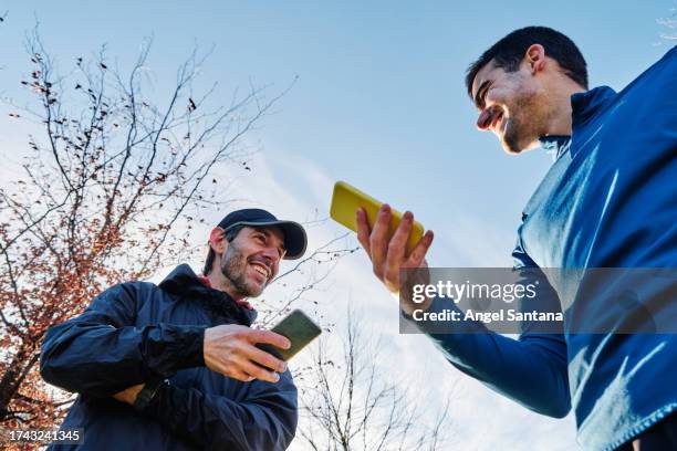 cheerful sportsmen comparing training results on smartphones - runners stock pictures, royalty-free photos & images