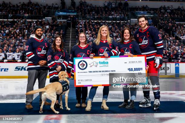 Adam Lowry of the Winnipeg Jets presents a cheque to members of the Toba Centre's multidisciplinary team during the pre-game ceremony prior to puck...
