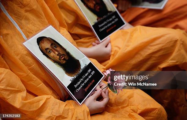 Supporters of closing the Guantanamo Bay Naval Base detention facility wearing orange prison style jumpsuits hold pictures of prisoners being held at...