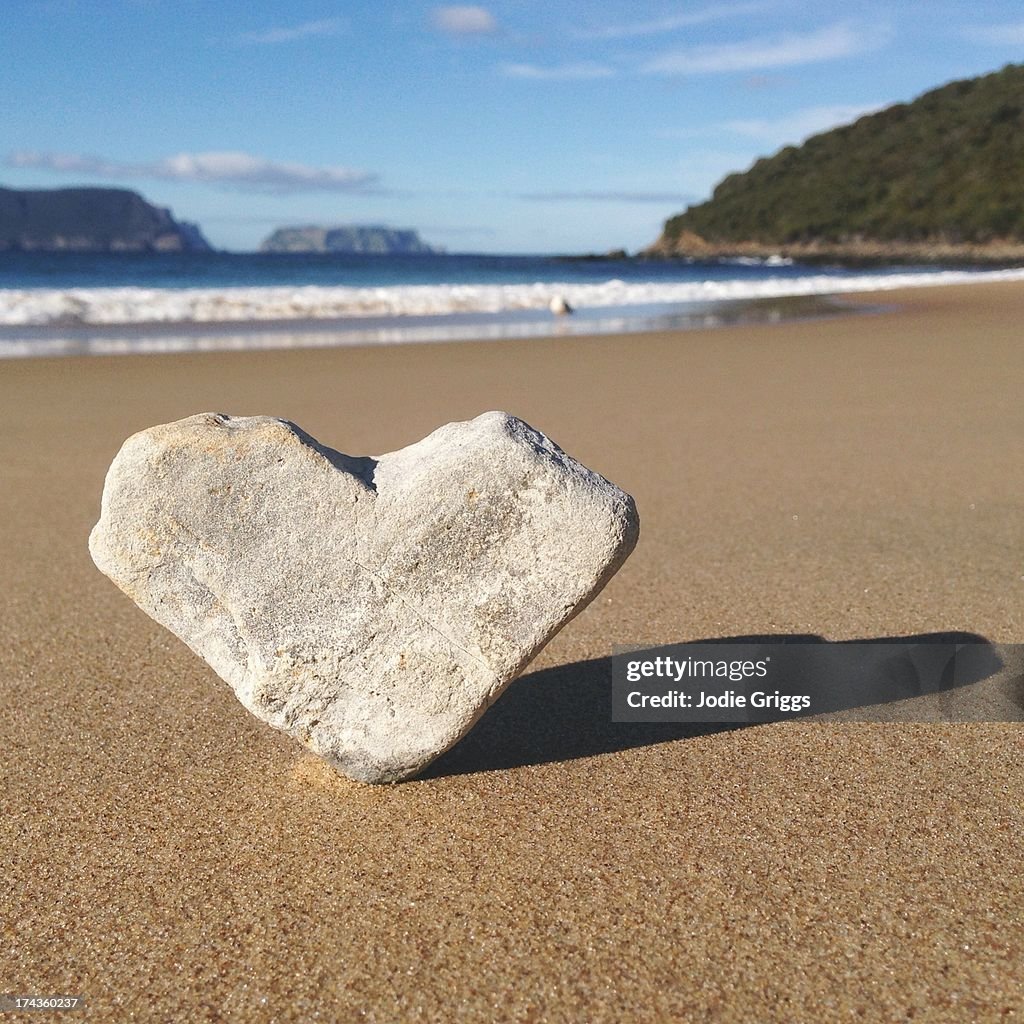 Heart shaped rock sitting in sand at the beach