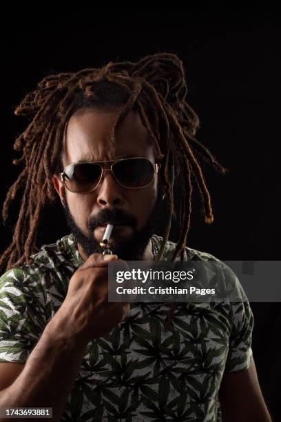 rasta man wearing weed tshirt lighting a marijuana cigarette black background - nuevo leon state stock pictures, royalty-free photos & images