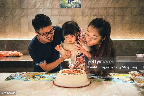 young couple & toddler blowing birthday candle - chinese birthday stock-fotos und bilder