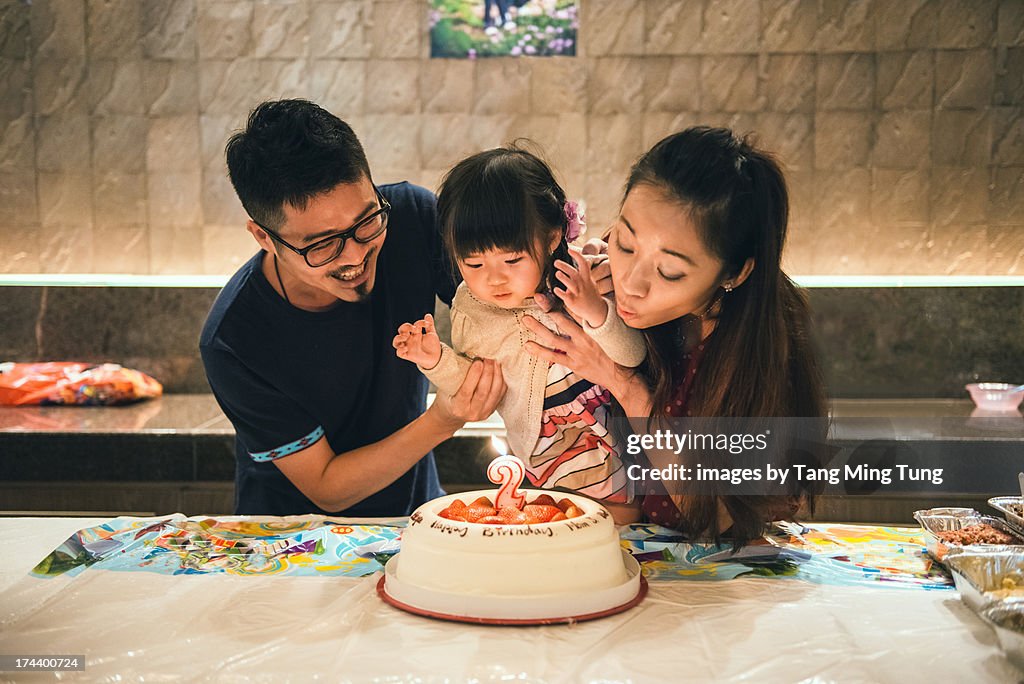 Young couple & toddler blowing birthday candle