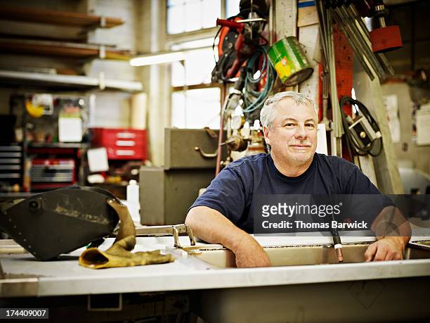 Smiling mature sheet metal worker sitting in shop