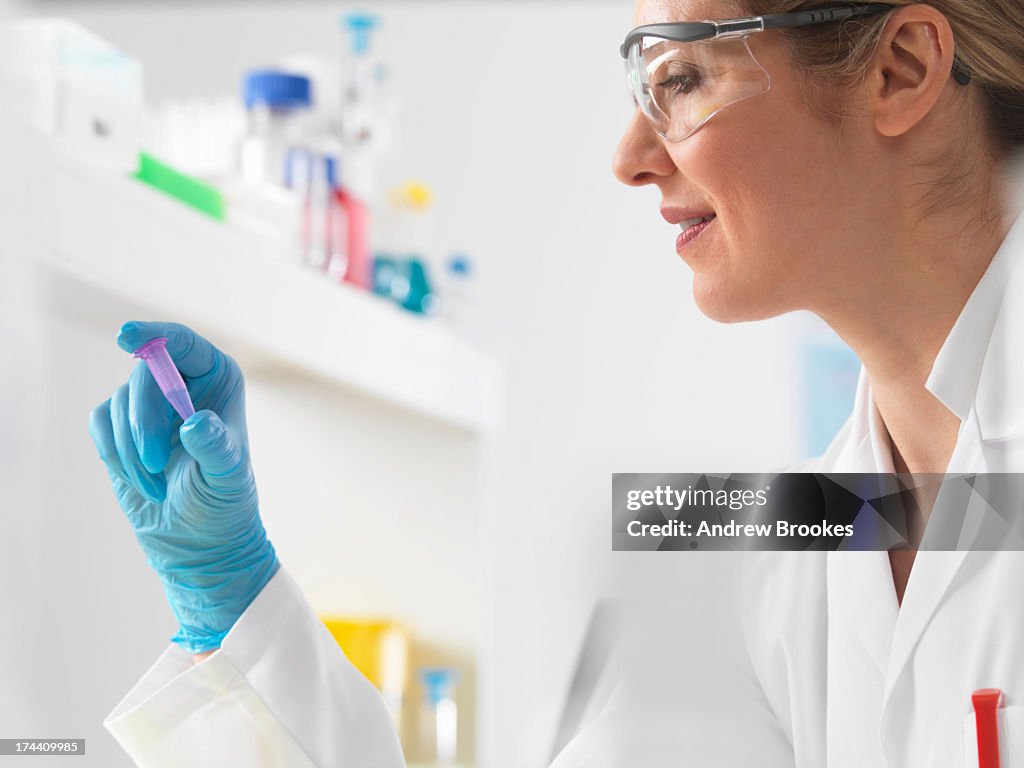 Female scientist viewing DNA sample in vial ready for testing in the laboratory