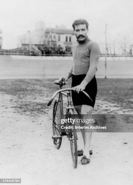 Portrait of French cyclist Leon Georget standing with his bicycle in the center of an unidentified outdoor velodrome, 1900s.