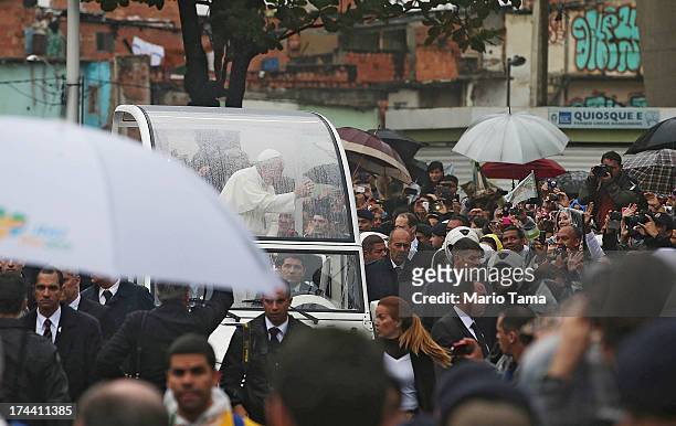 Pope Francis waves to the crowd while riding in the Popemobile as he tours the Varghina favela, or shantytown, on July 25, 2013 in Rio de Janeiro,...