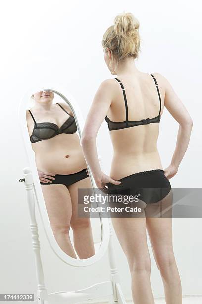 slim girl looking at fat reflection in mirror - women in slips stock-fotos und bilder
