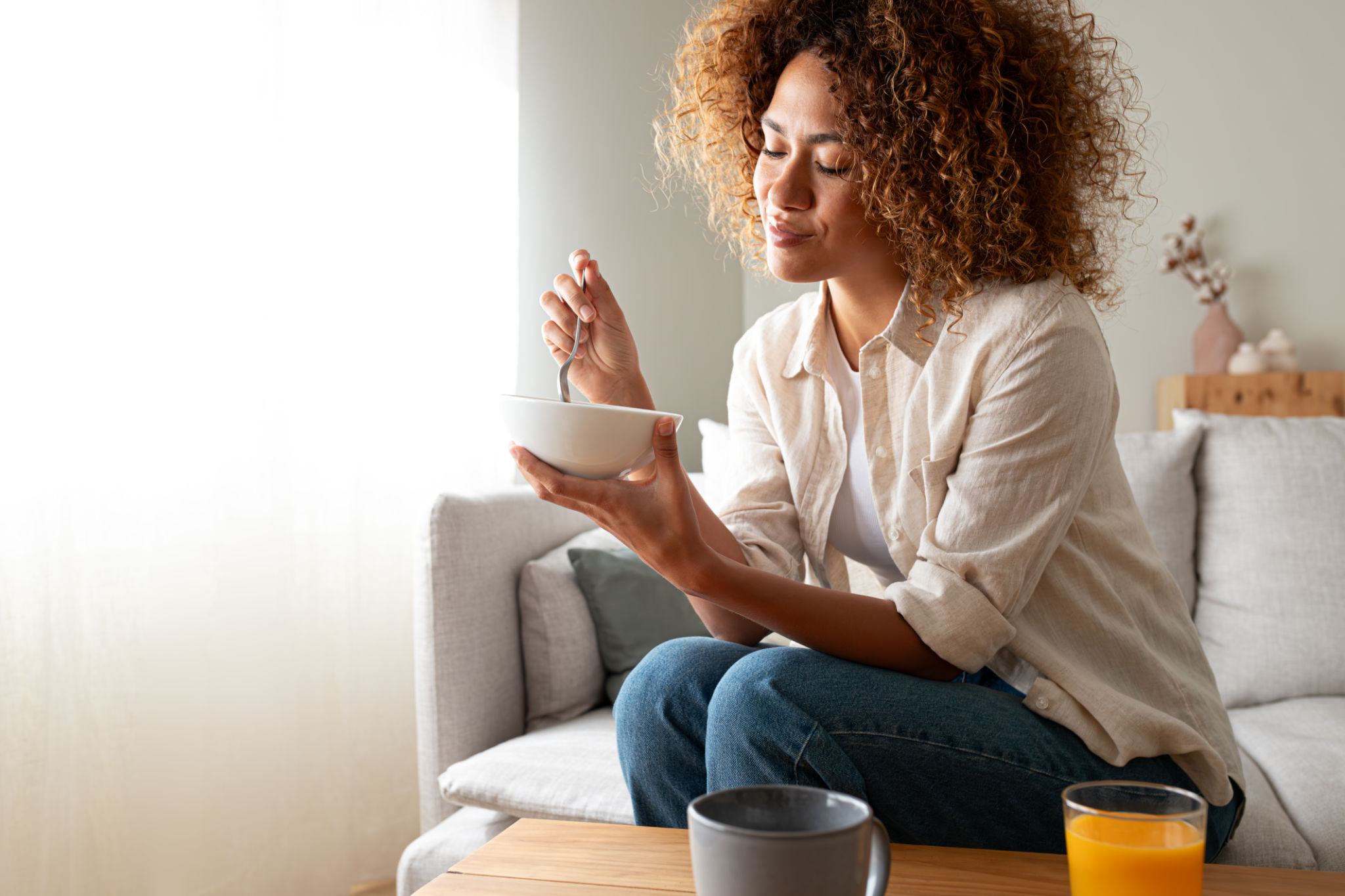 Young relaxed pensive African American woman eating healthy breakfast sitting on the couch. Copy space. Young relaxed pensive African American woman eating healthy breakfast sitting on the couch. Copy space.