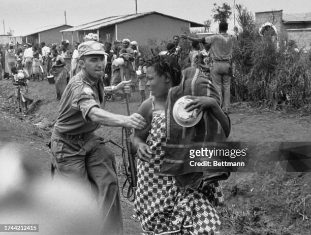 Baluba woman, carrying her baby wrapped in a blanket, is grabbed by a UN soldier after leaving the queue during food distribution at a refugee camp...