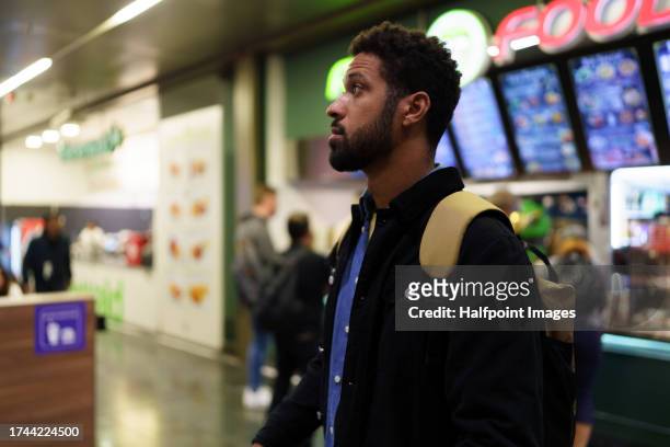 young man standing alone in a food court, choosing what to eat for dinner. single man going to dine in a shopping mall in the city. - man eating at diner counter foto e immagini stock