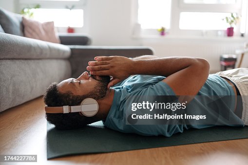 The single man meditating alone at home while listening to meditation music through wireless headphones, doing breathing exercises. The single man meditating alone at home while listening to meditation music through wireless headphones, doing breathing exercises.