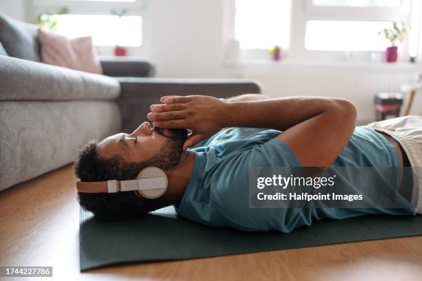 the single man meditating alone at home while listening to meditation music through wireless headphones, doing breathing exercises. - wohlbefinden stock-fotos und bilder