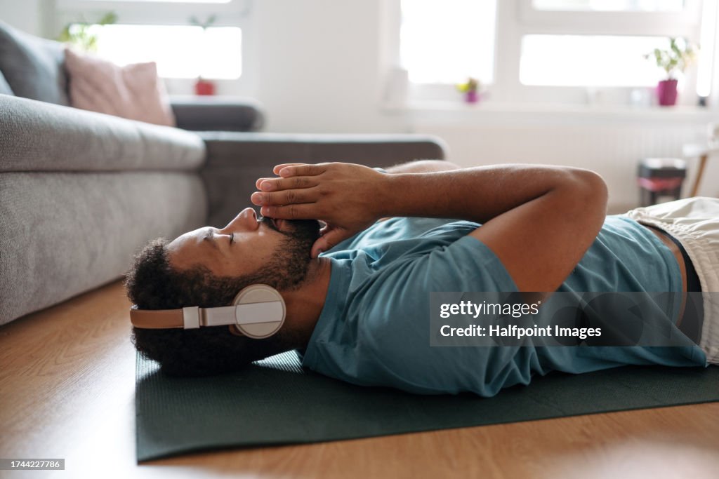The single man meditating alone at home while listening to meditation music through wireless headphones, doing breathing exercises.