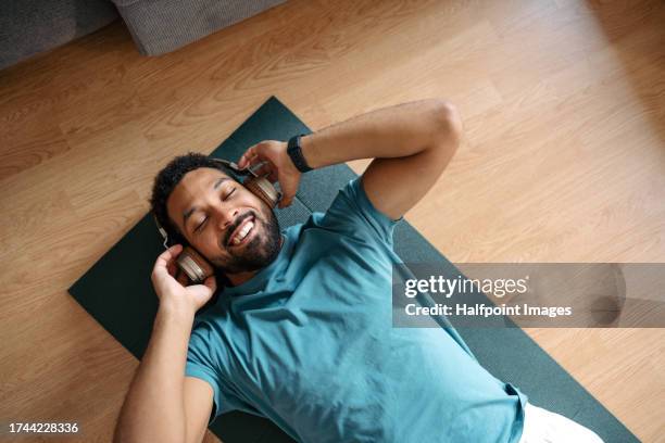 the single man exercising alone at home while listening to music through wireless headphones. young man is happy, relaxed, and content with his life. solo home workout and meditation, morning or evening workout routine. - fitnesstraining stock-fotos und bilder