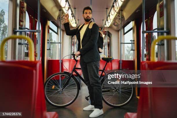 stylish man standing in a city train holding his bicycle, which he uses to commute around the city. single man traveling home by public transport after long workday. - commuter train stock pictures, royalty-free photos & images