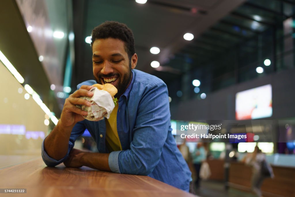 Handsome man eating alone outdoors, enjoying fast food in the city. Single man eating simple dinner alone, relishing the city hustle.