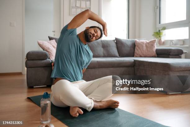 the single man exercising alone at home, stretching his back and arm. young man is happy, relaxed, and content with his life. solo home workout and meditation, morning or evening workout routine. - estirándose fotografías e imágenes de stock