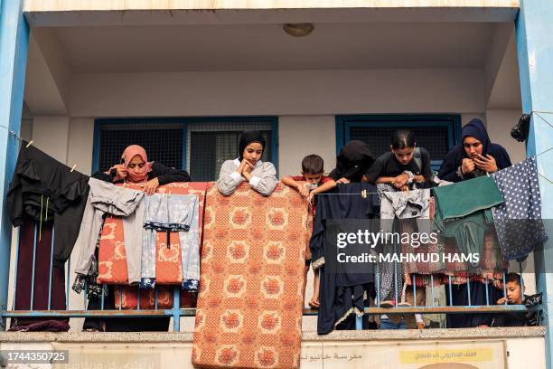 Woman and children stand before a mattress and laundry drying out on a balcony walkway outside a classroom that has been converted into a make-shift...